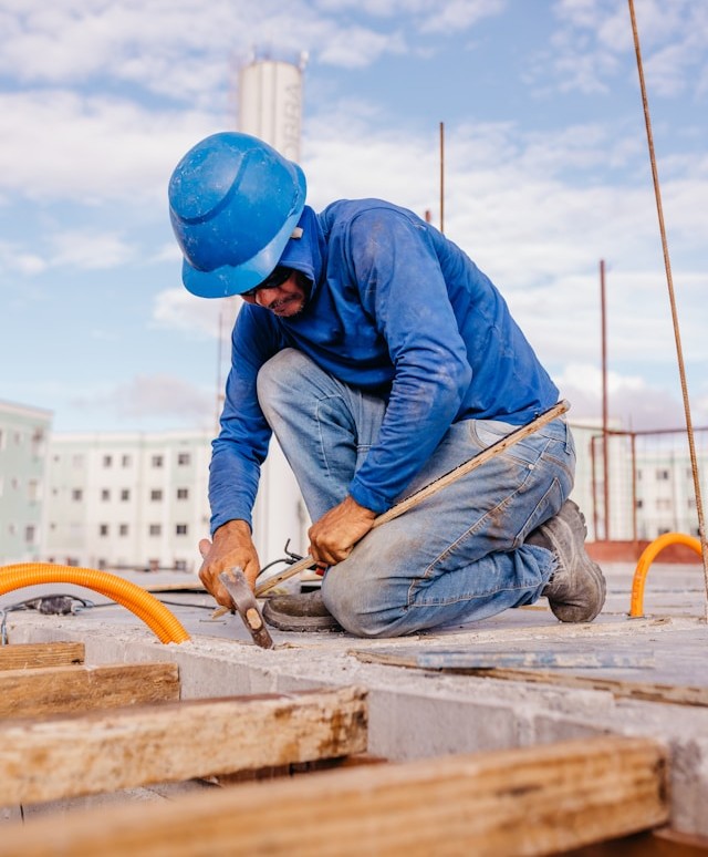 A Construction Worker Carrying Metal Beam With Crane in Background